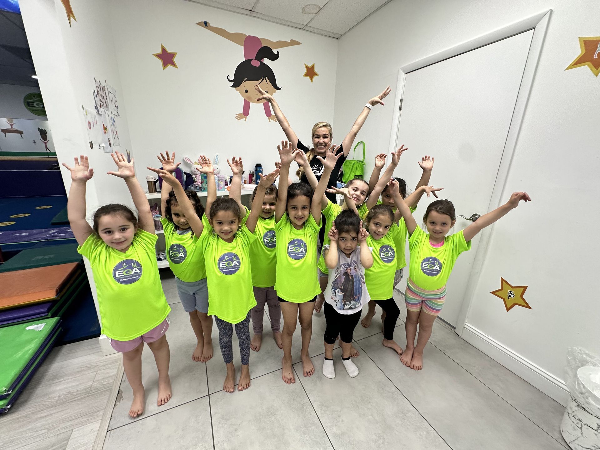 Un grupo de chicas jóvenes están de pie en una habitación con las manos en el aire.