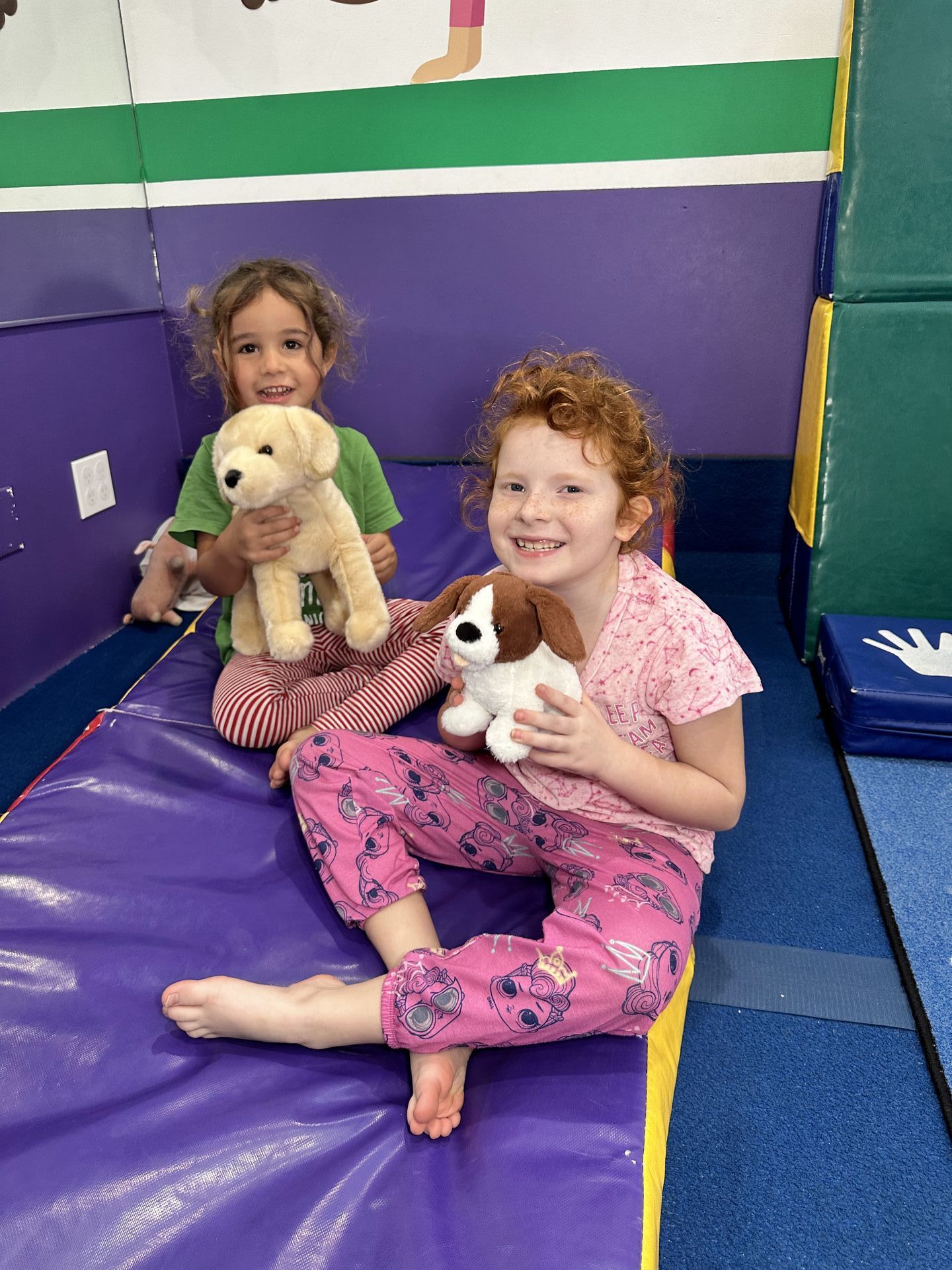 Dos niñas están sentadas en una estera sosteniendo animales de peluche.