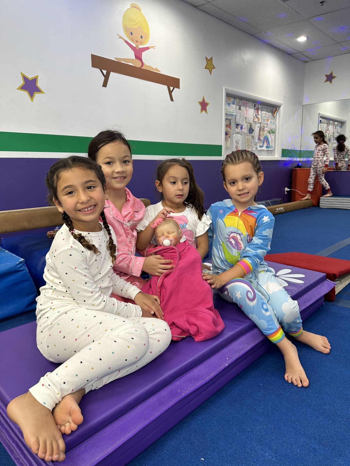 Un grupo de chicas jóvenes están sentadas en una colchoneta morada en un gimnasio.
