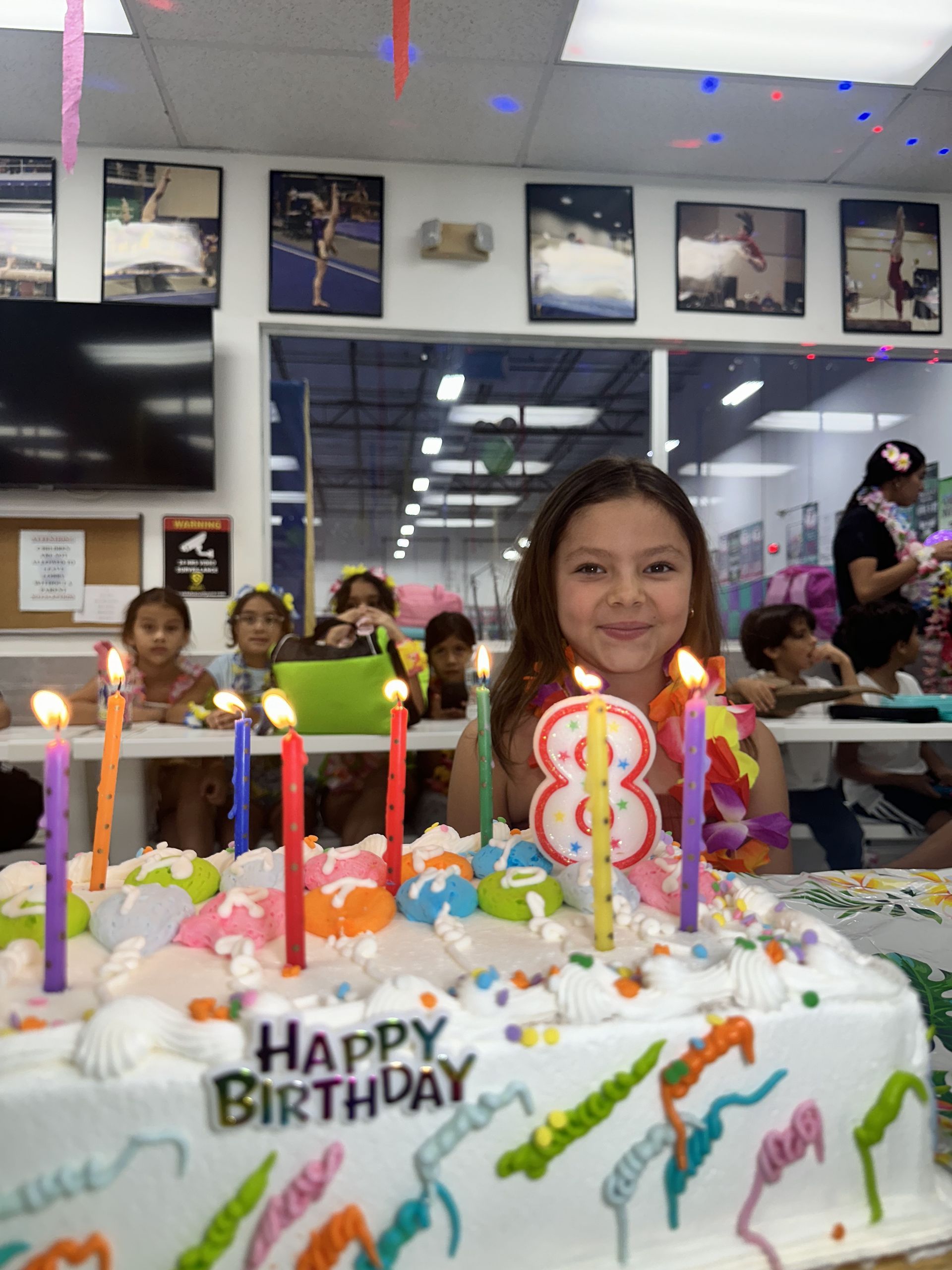 Una niña está sentada delante de un pastel de cumpleaños con velas.