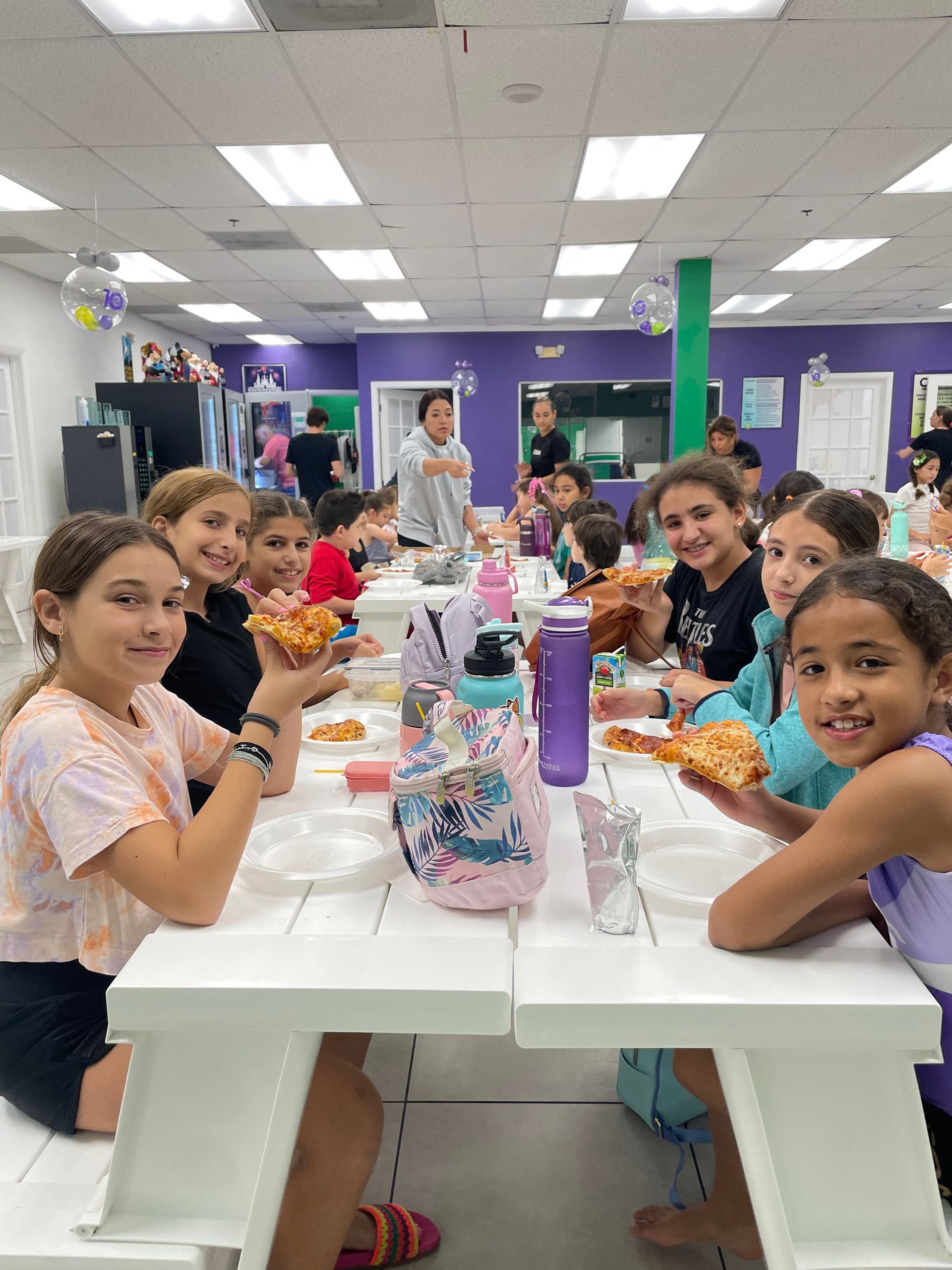Un grupo de chicas jóvenes están sentadas en una mesa larga comiendo pizza.
