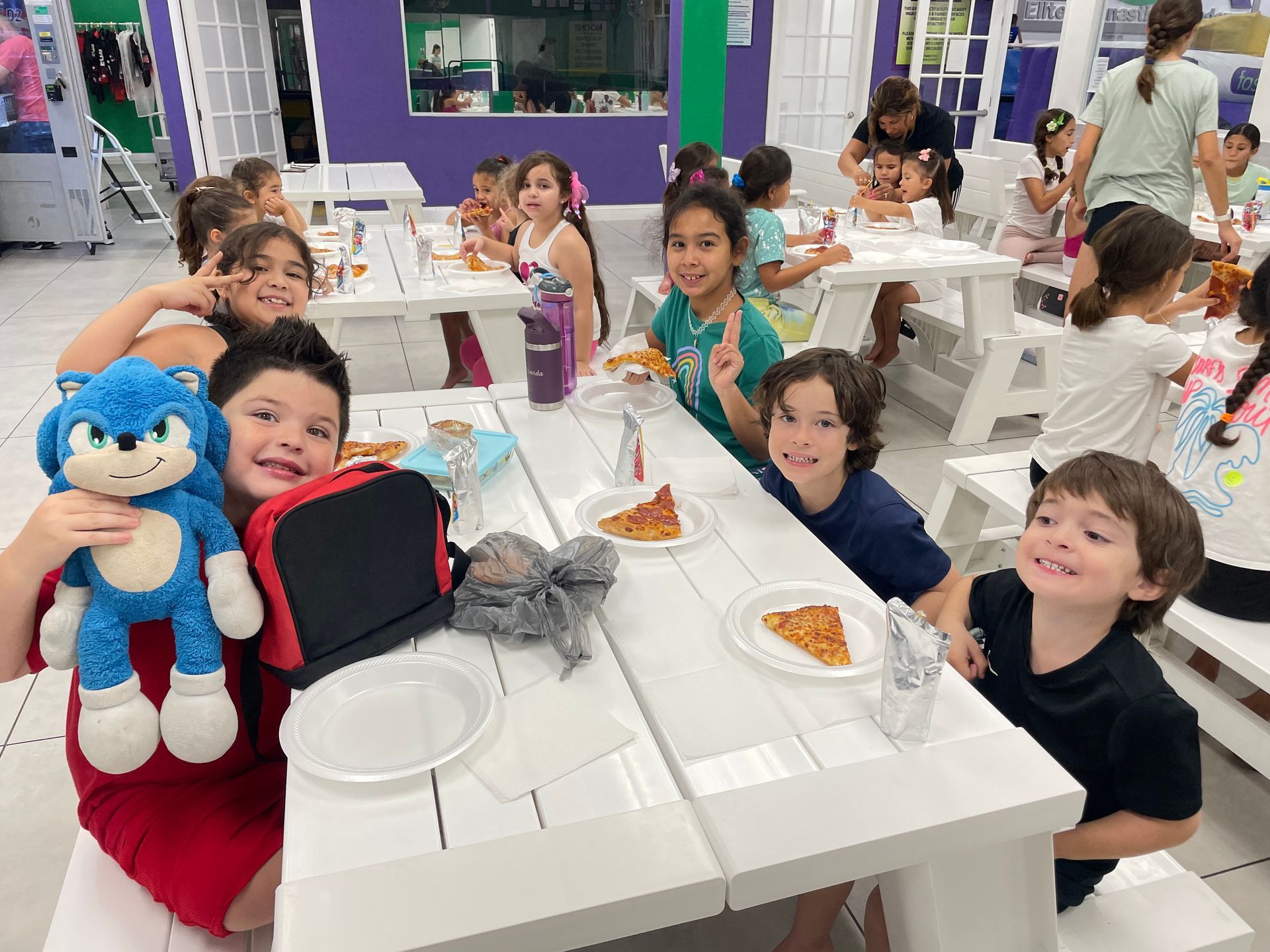 Un grupo de niños está sentado en una mesa comiendo pizza.