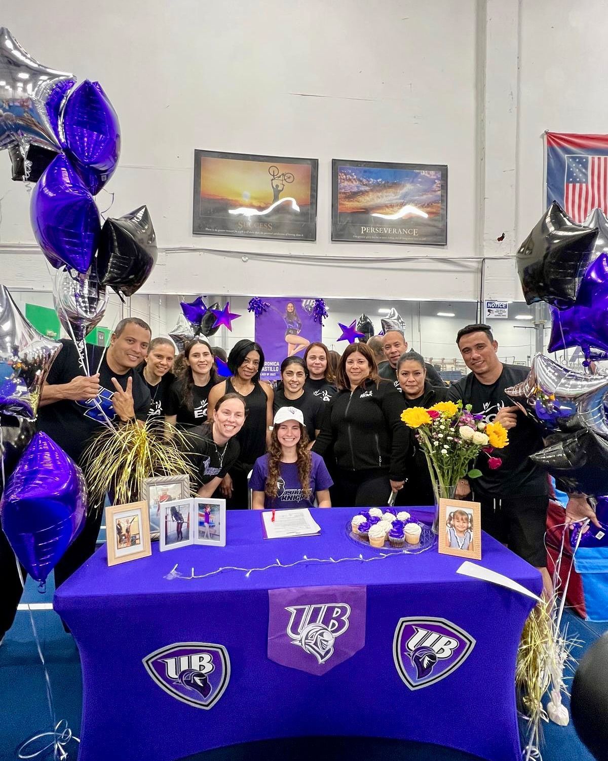 Un grupo de personas están de pie alrededor de una mesa con globos y flores.