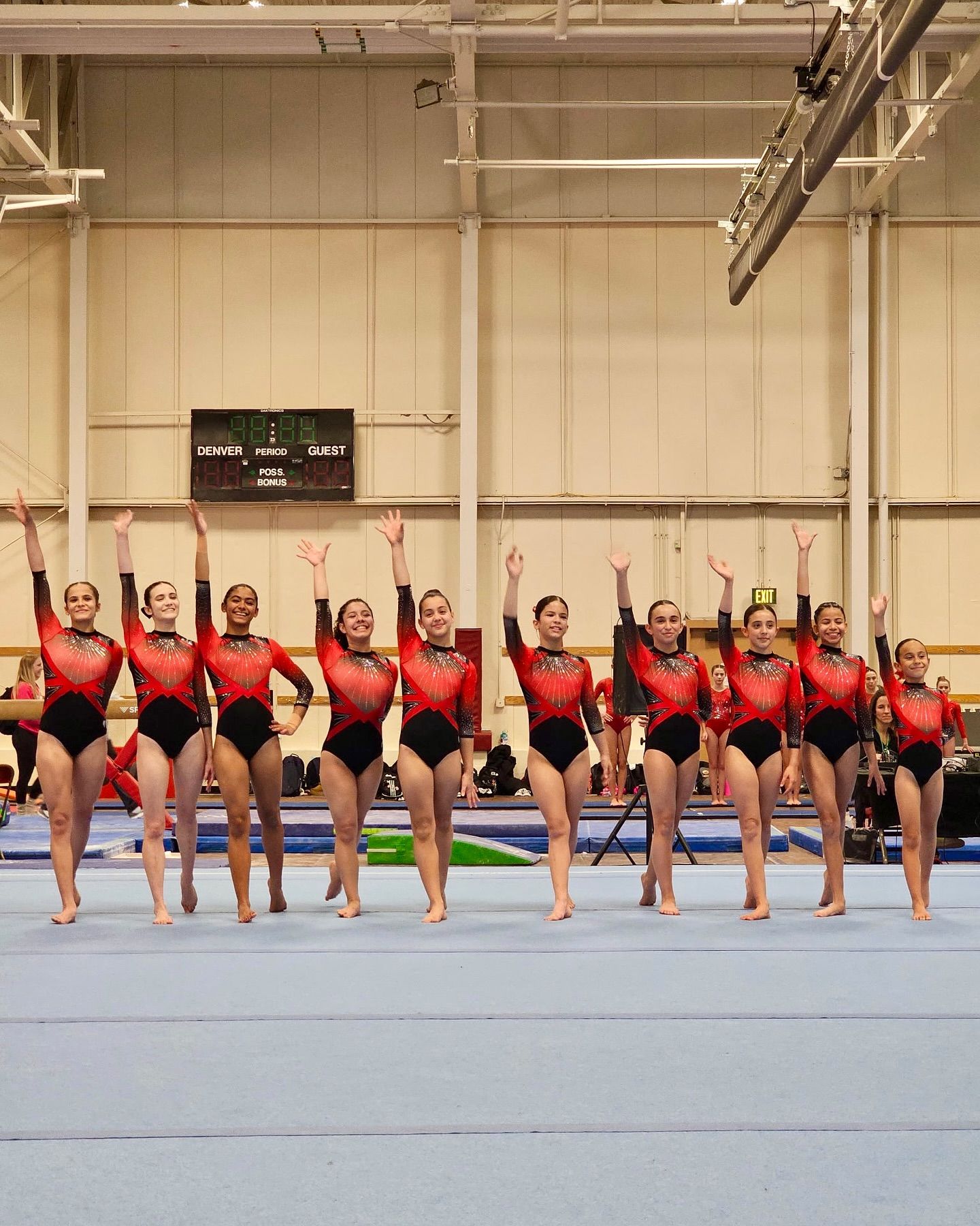 Un grupo de gimnastas femeninas están de pie sobre una colchoneta azul en un gimnasio.