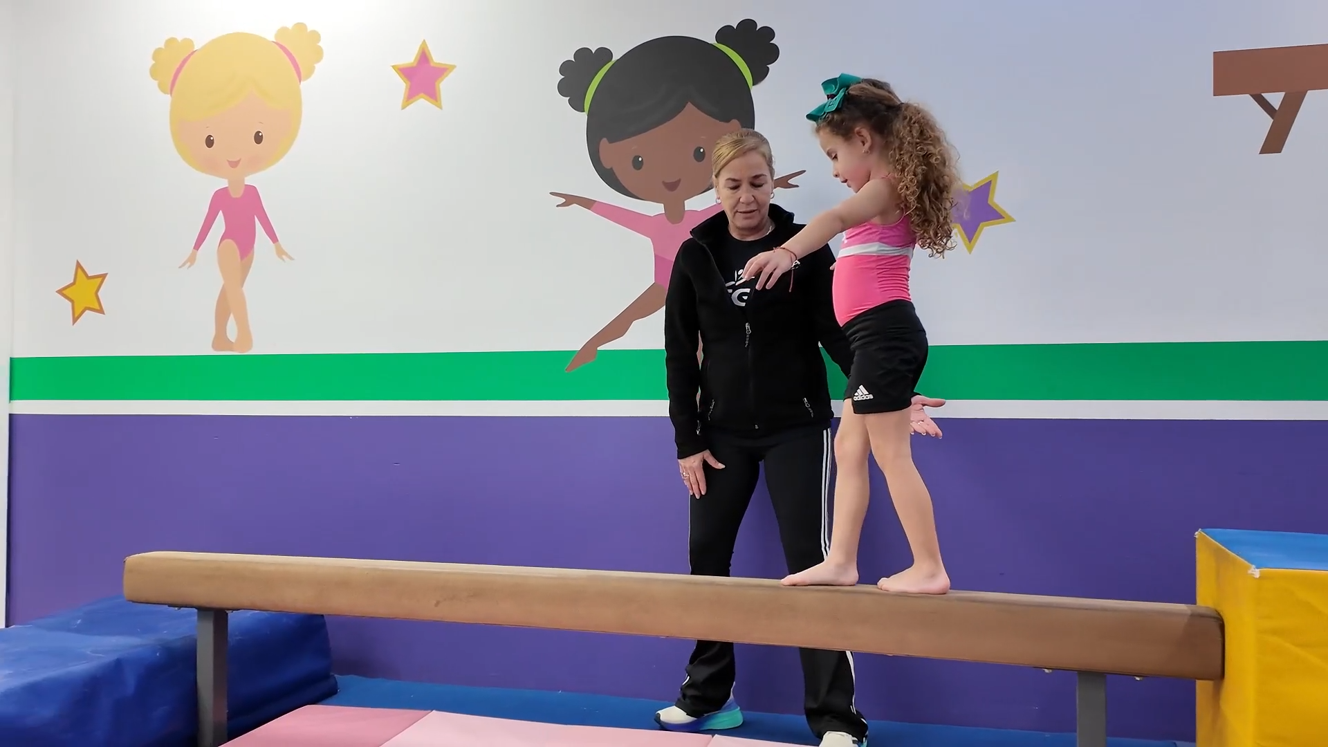 Una mujer está ayudando a una niña a mantener el equilibrio en una viga de equilibrio.