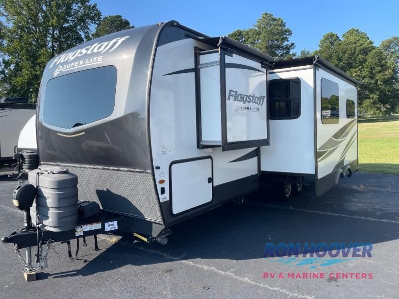 A white and black Flagstaff travel trailer with an open slide-out in an outdoor setting.