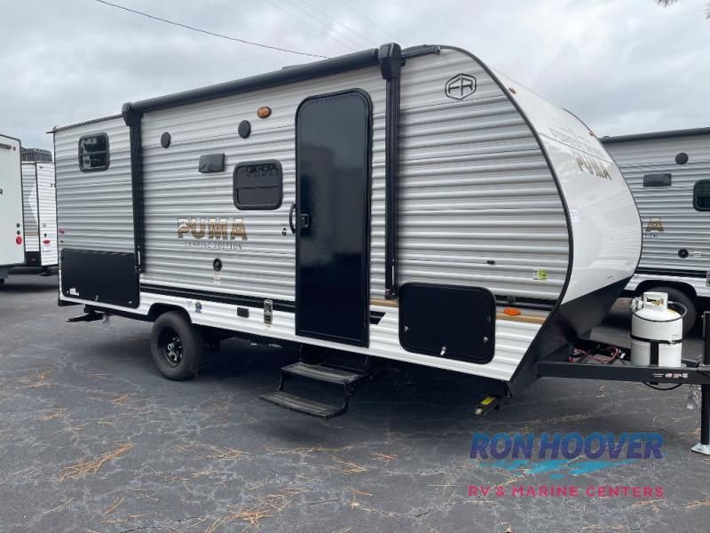 Gray and white Puma travel trailer with awning and black door, parked outside.