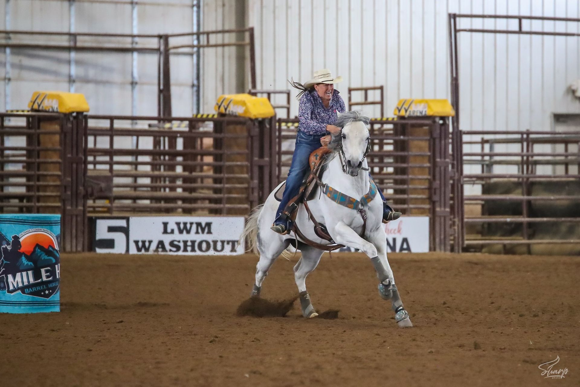 A woman is riding a white horse in a rodeo arena.