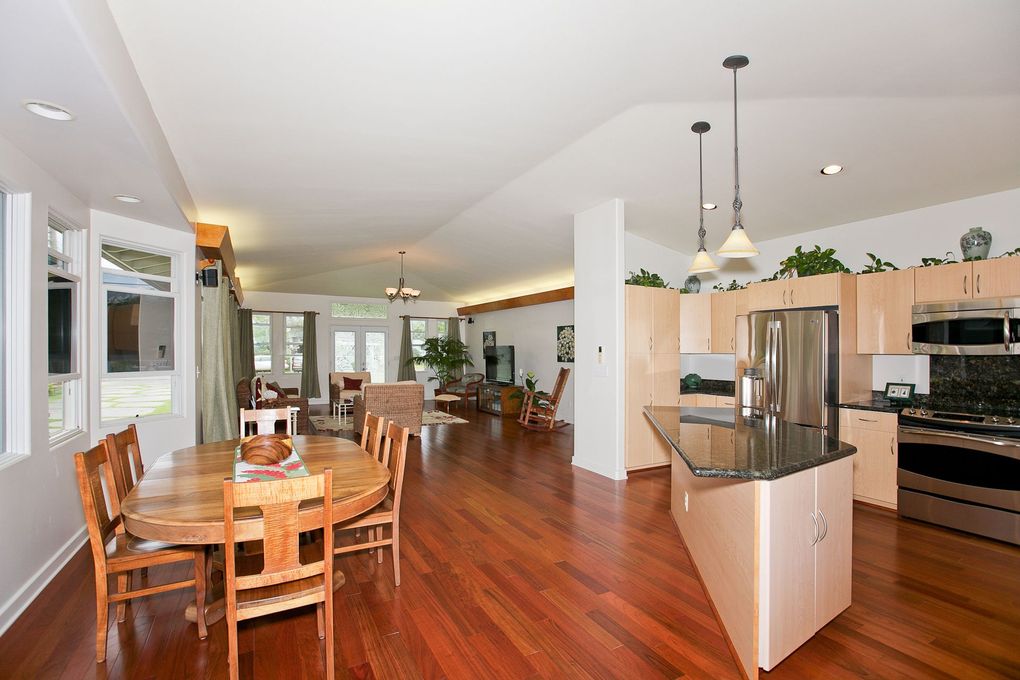 An open-concept dining area and kitchen with hardwood floors, a round wooden table, and stainless steel appliances.