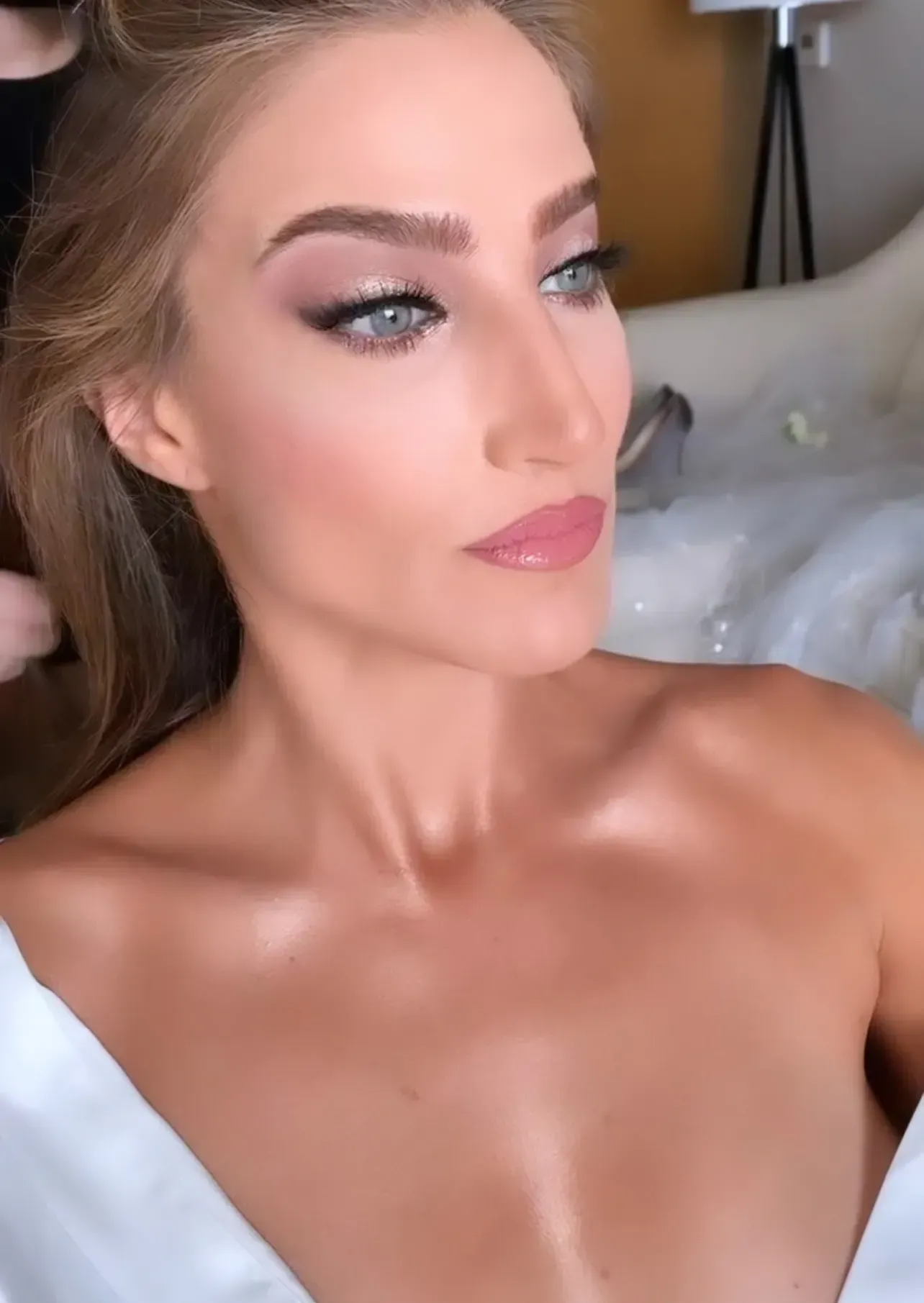 Woman with elegant makeup, looking away, wearing a white robe.