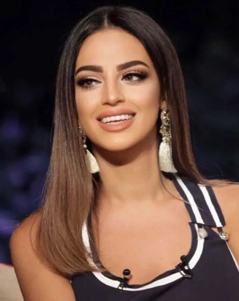 Woman with long, ombre hair, wearing a dark top with white stripes, smiling, and wearing dangling earrings.