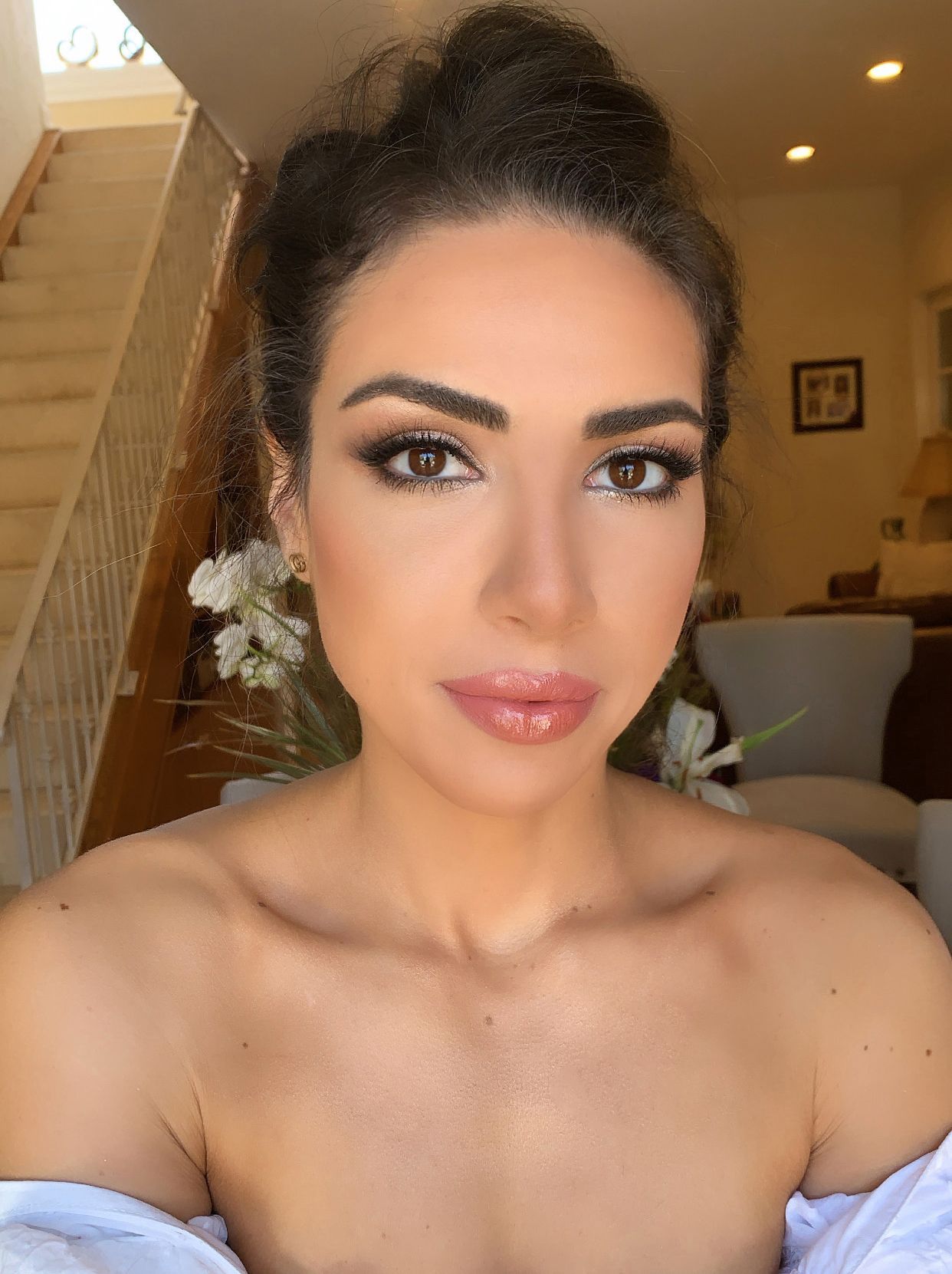 Woman with dark hair and makeup, off-the-shoulder top, indoors.