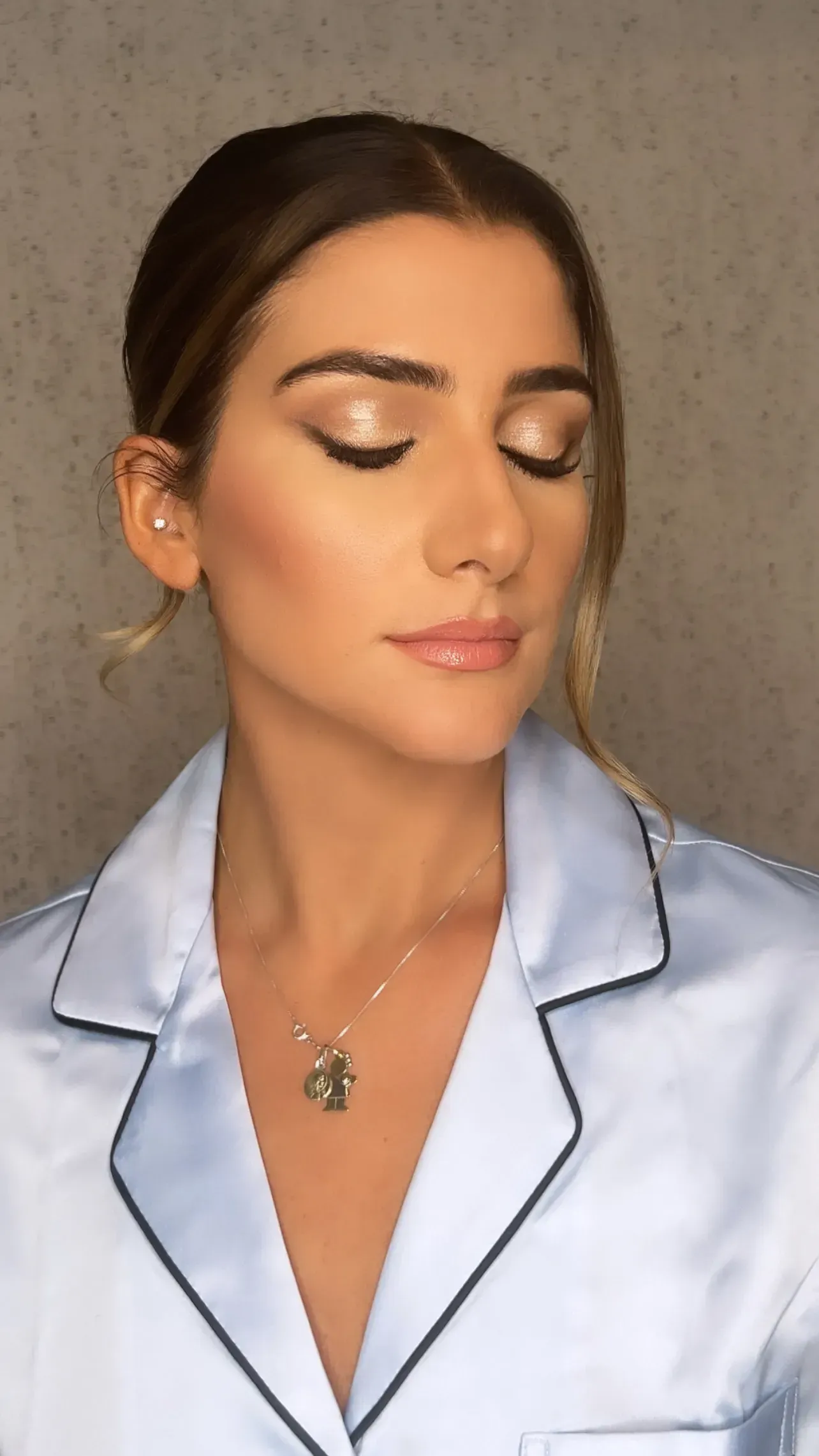 Woman with light makeup wearing blue satin pajamas, eyes closed, lit by soft light.