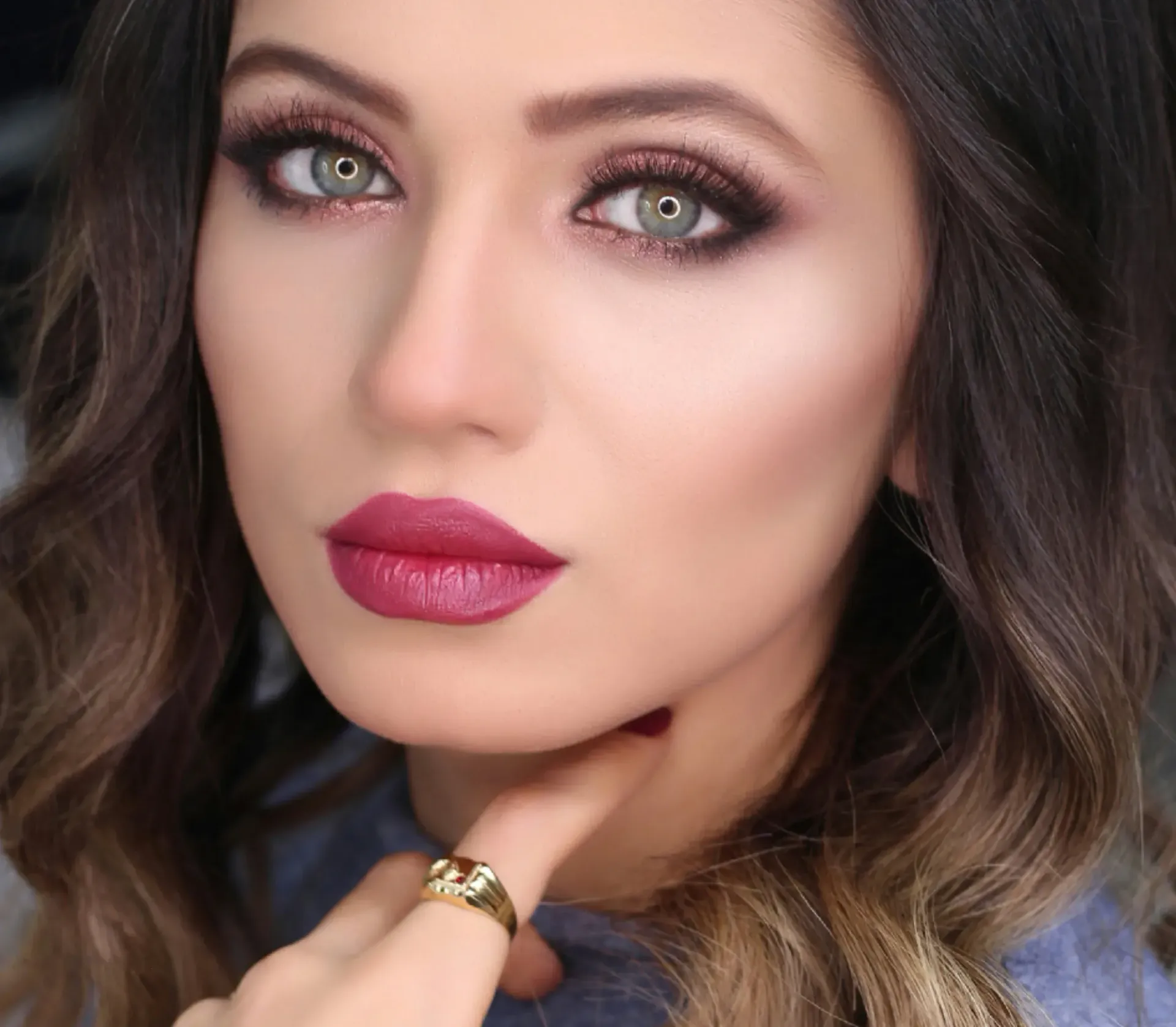 Woman with dark hair and bold makeup: smoky eye, red lipstick, gold ring, fair skin.