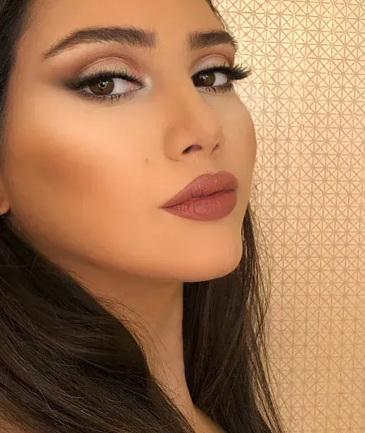 Woman with brown hair and professional makeup: smoky eyes, nude lips, and contoured cheeks.