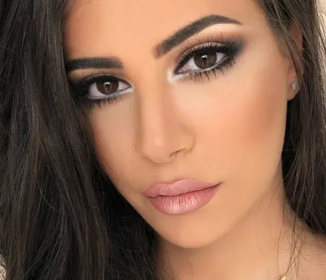 Woman with dark hair and dramatic eye makeup, including smoky eyes and full lips, with highlighted cheeks.