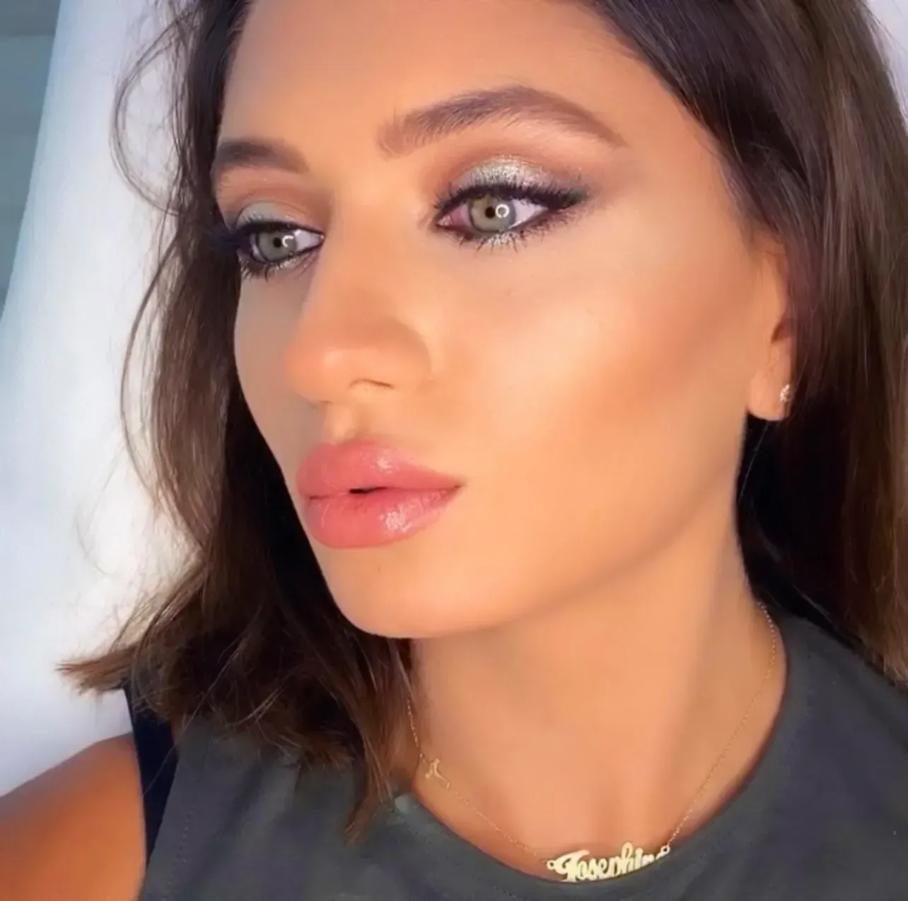 Woman with dramatic eye makeup, looking slightly up. She has light skin, full lips, and is wearing a necklace.