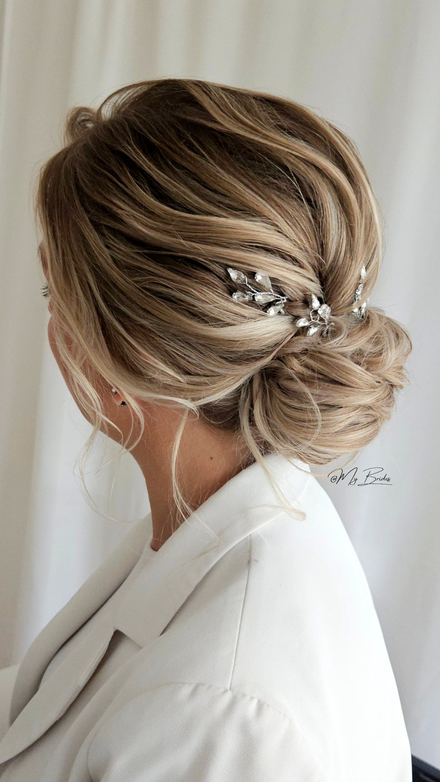 Bruidskapsel voor een moderne bruid met haarsieraden, laag opgestoken met structuren
