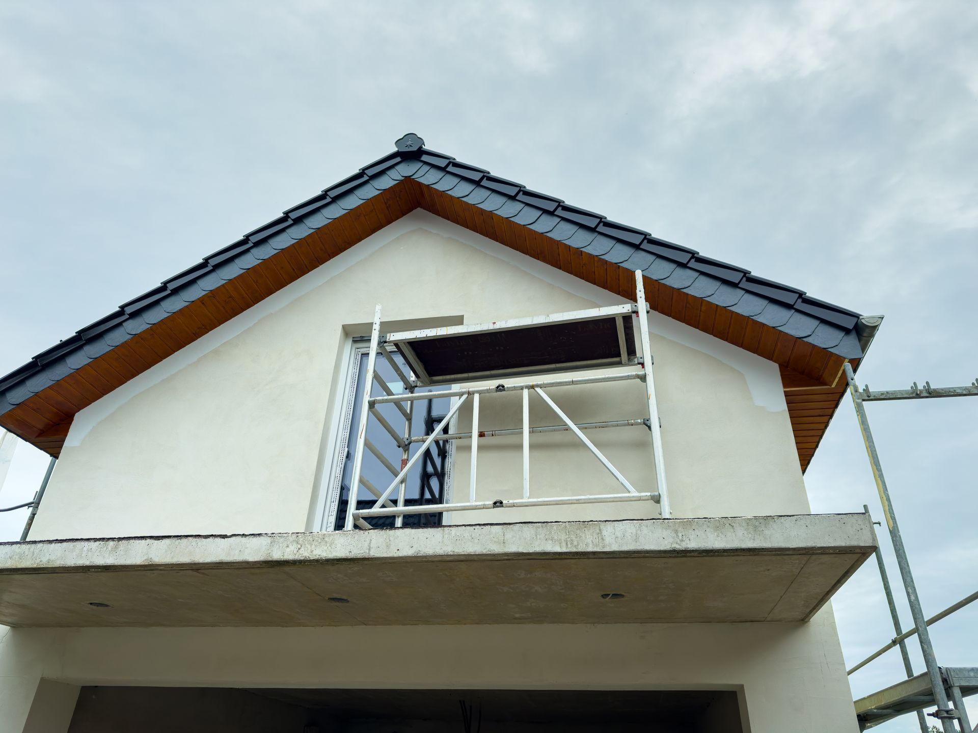House exterior under construction, with scaffolding at a window and a roof with gray tiles.