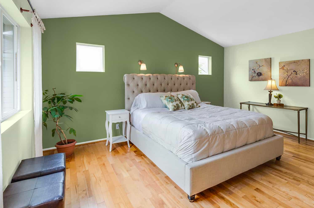 Bedroom with green accent wall, tufted headboard, wooden floor, and natural light.
