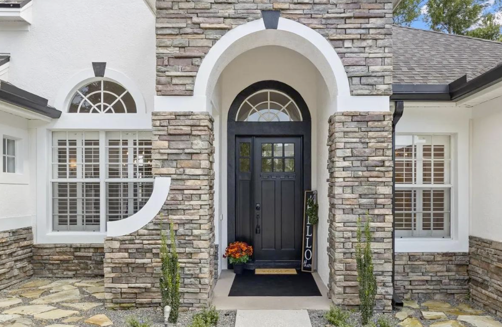 Tan stucco home with stone entry, palm trees, blue sky.