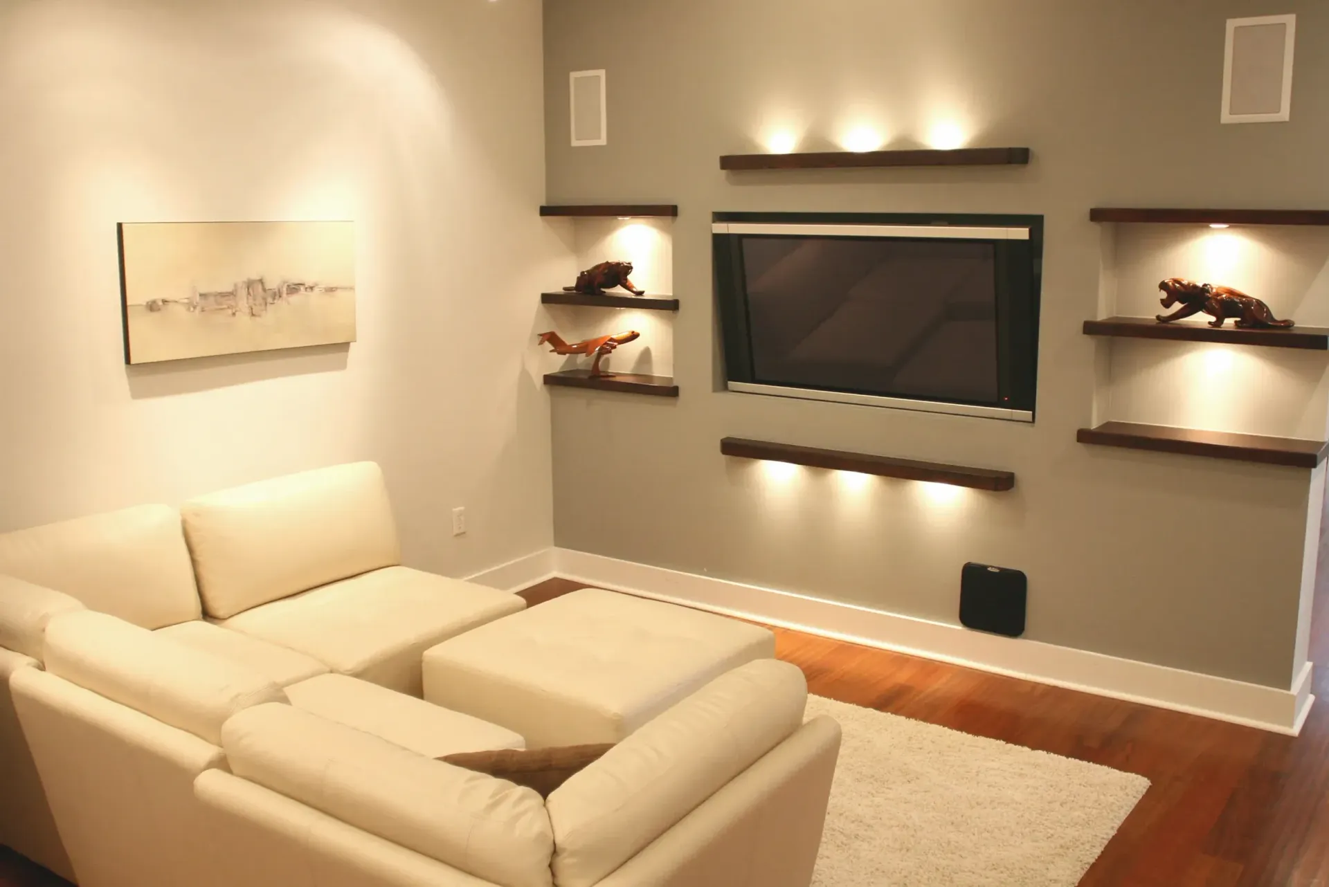A modern living room with a sectional sofa, built-in TV, shelves, and warm lighting.