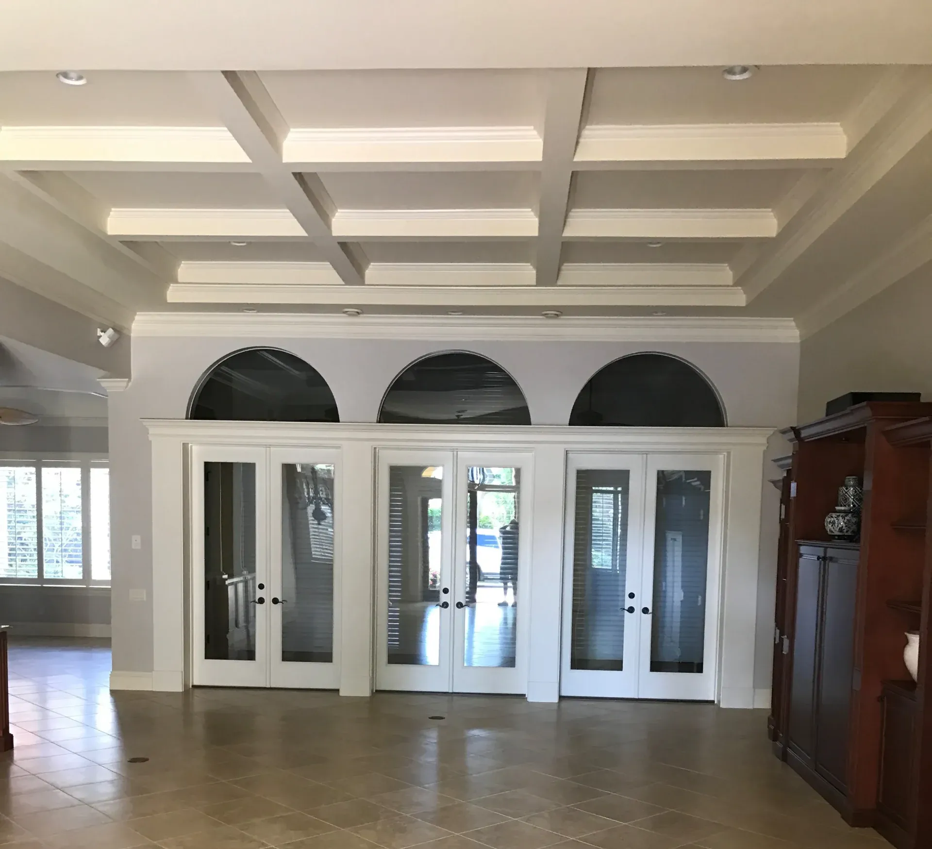 Interior view: Three white double doors beneath arches, topped by a coffered ceiling.