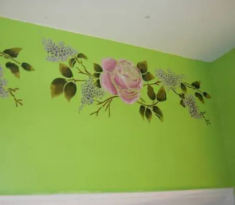 Floral wall stencil with a pink rose and lavender-colored blossoms on a bright green wall.