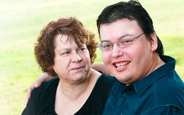 A woman looking toward a smiling person in glasses, outdoors in a green, grassy setting.
