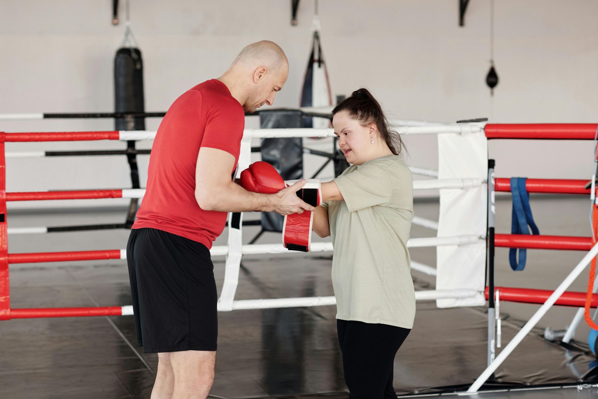A trainer helps an athlete put on red boxing gloves inside a boxing ring.