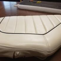 Cream-colored boat seat with black piping and vertical stitched panels on a brown wooden table.