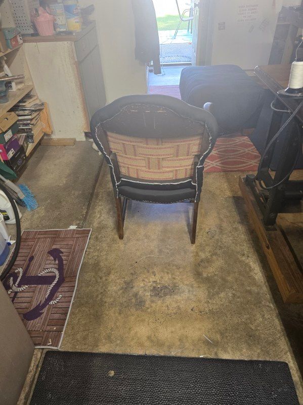 An old wicker rocking chair sits on a concrete floor in a cluttered room.