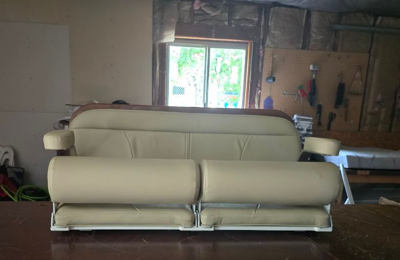 Cream-colored wingback chair with wooden frame on patterned rug near a window and potted plants.