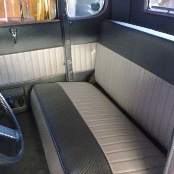 Interior of a classic car with a black and beige bench seat and beige side panels.