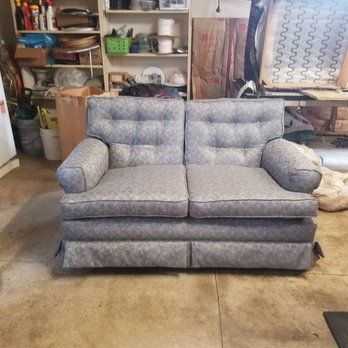 Gray patterned loveseat in cluttered workshop setting.