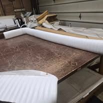 A work table with white foam tubing and rolled insulation in a garage-like setting.