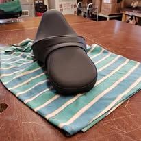 Black motorcycle seat on a striped blue and green cloth, placed on a wooden table.