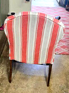 Man adjusting a beige pillow on an upholstered armchair. He's in a room with a window and concrete walls.