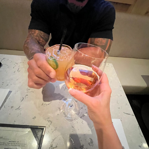 A man and a woman are toasting with drinks at a table