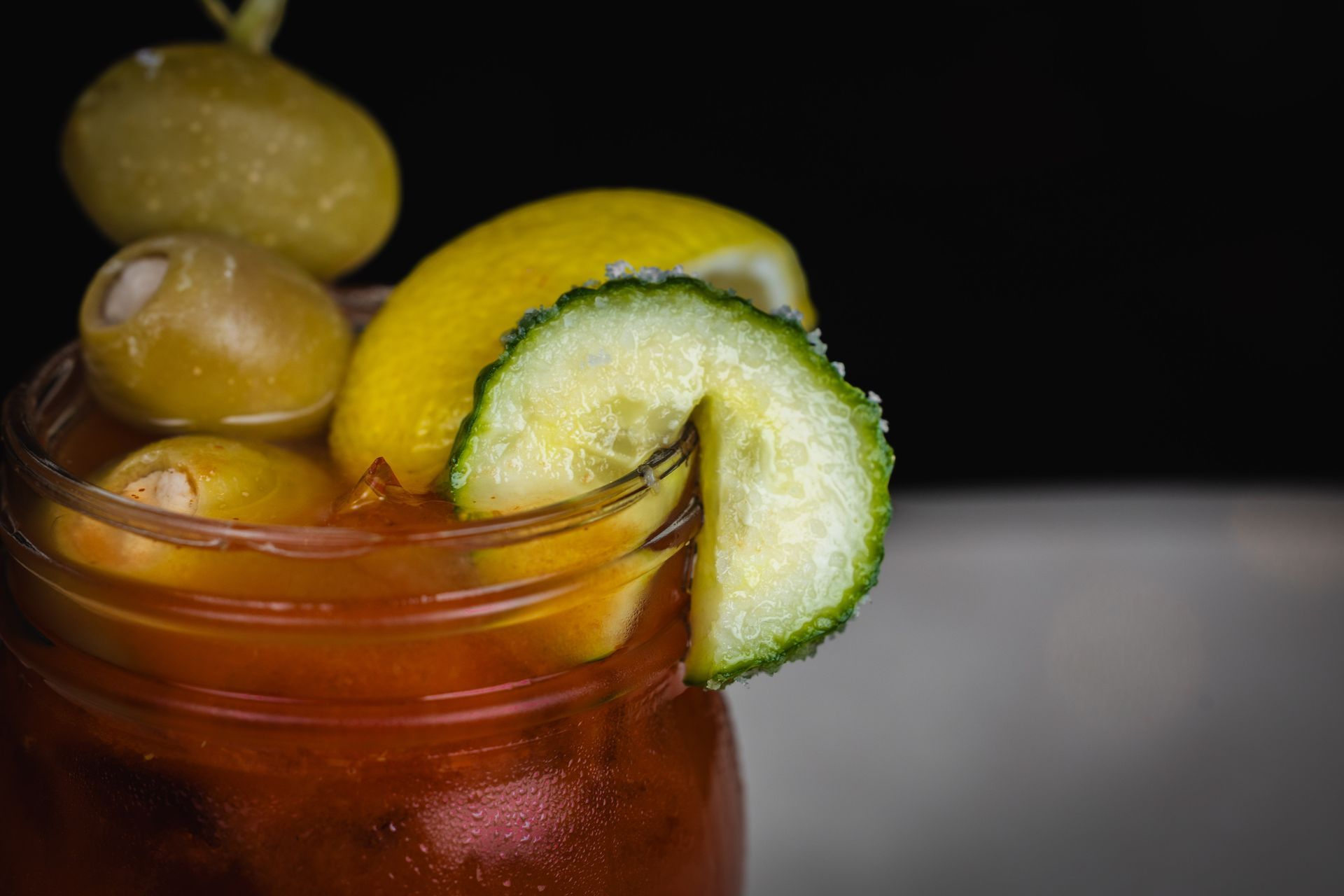 Desperato Bloody Mary cocktail in a glass jar, garnished with olives, lemon, and salted cucumber slice.