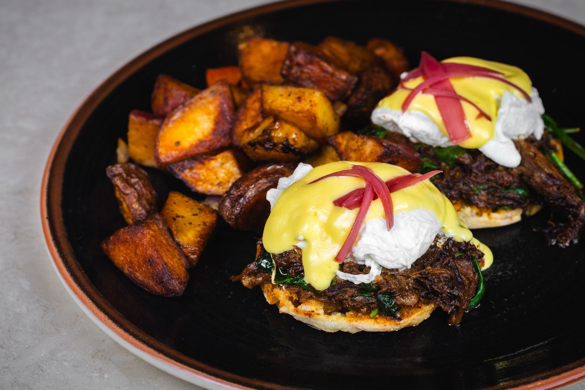 Eggs Benedict with roasted potatoes on a black plate.