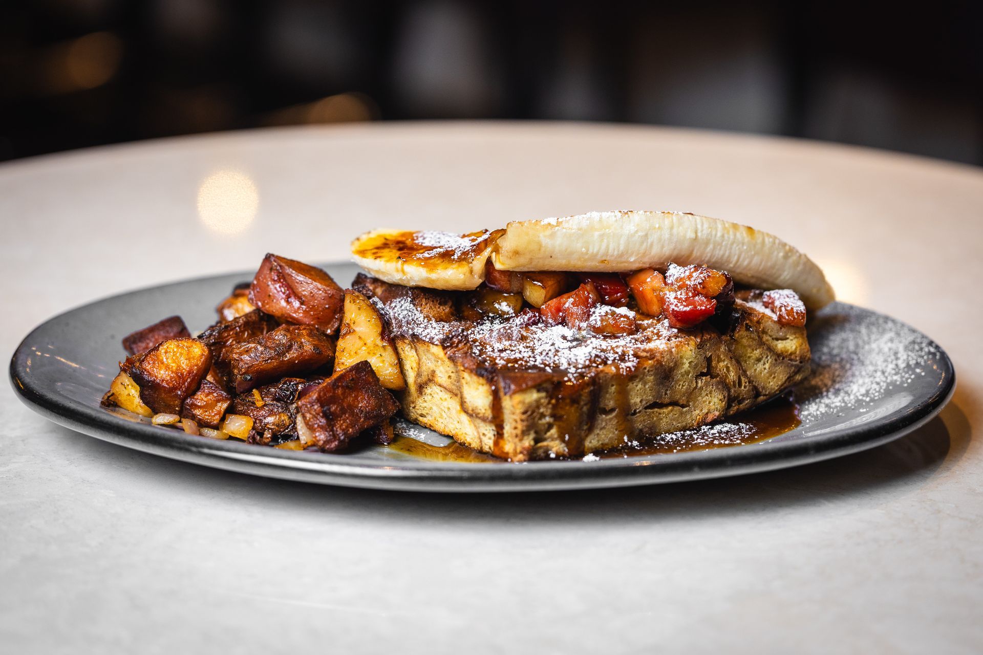 French toast with fried banana and fruit garnish on a gray plate.