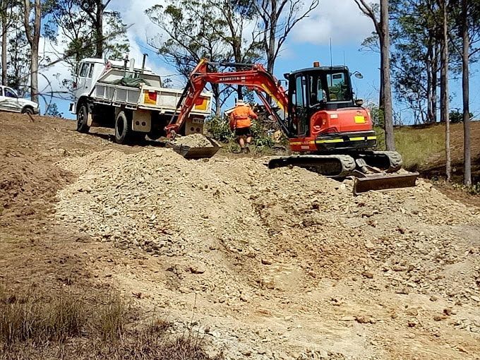 A Truck And An Excavator Are Working On A Dirt Road — Ant's Earthworks In North Deep Creek, QLD 