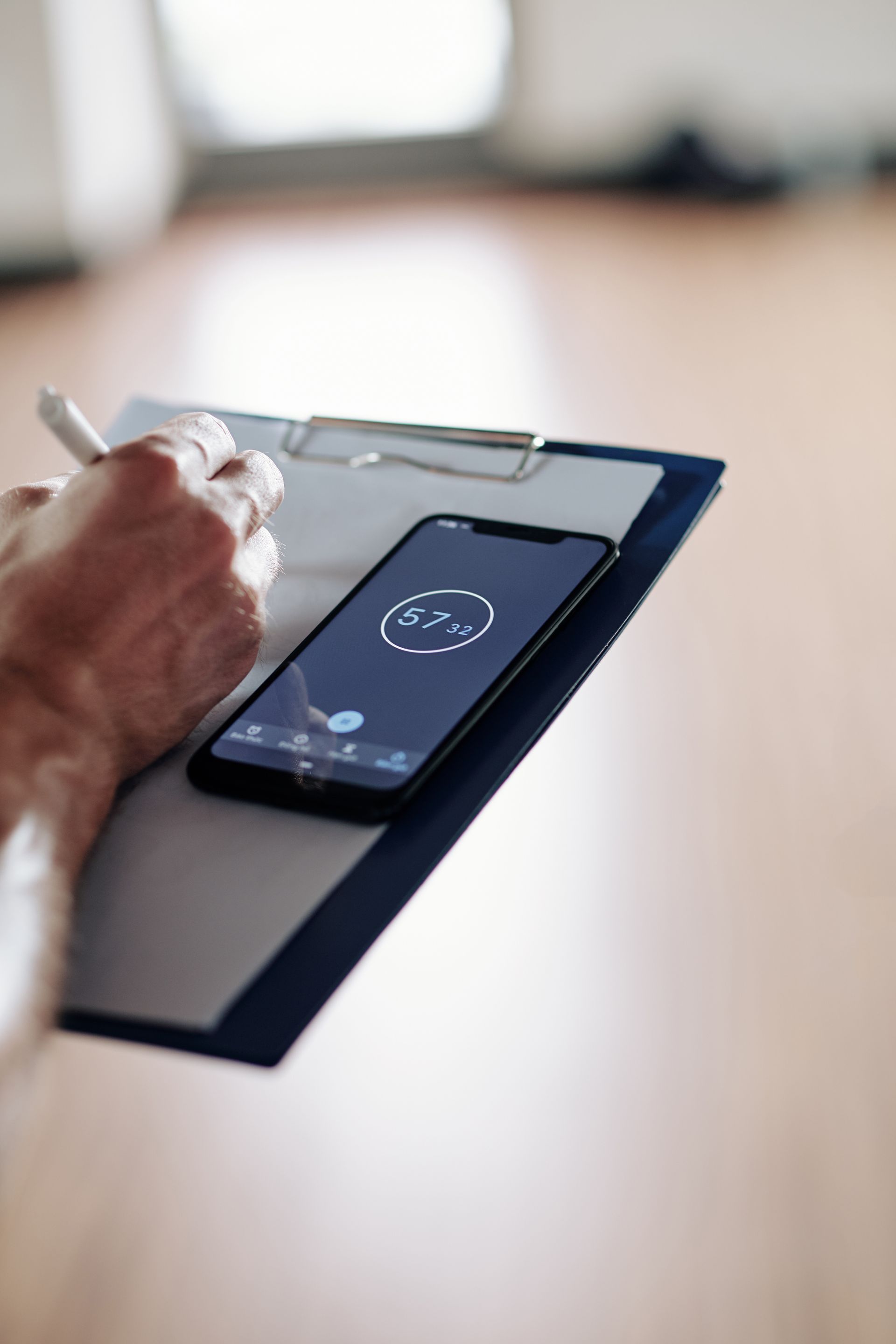 Person som skriver på ett urklipp, med en smartphone som visar en timer ovanpå.