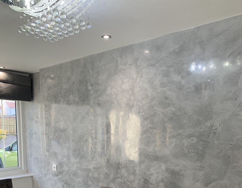Gray textured wall, reflective surface, with chandelier and recessed lighting in a room.