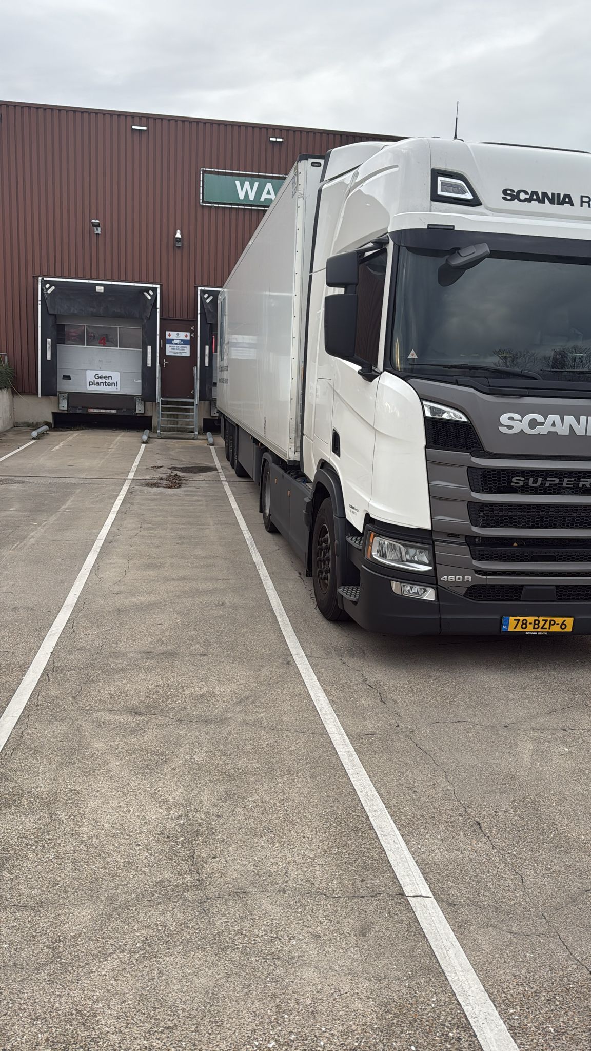 Een witte vrachtwagen staat geparkeerd bij een laadperron; een tweede laadperron is links zichtbaar.