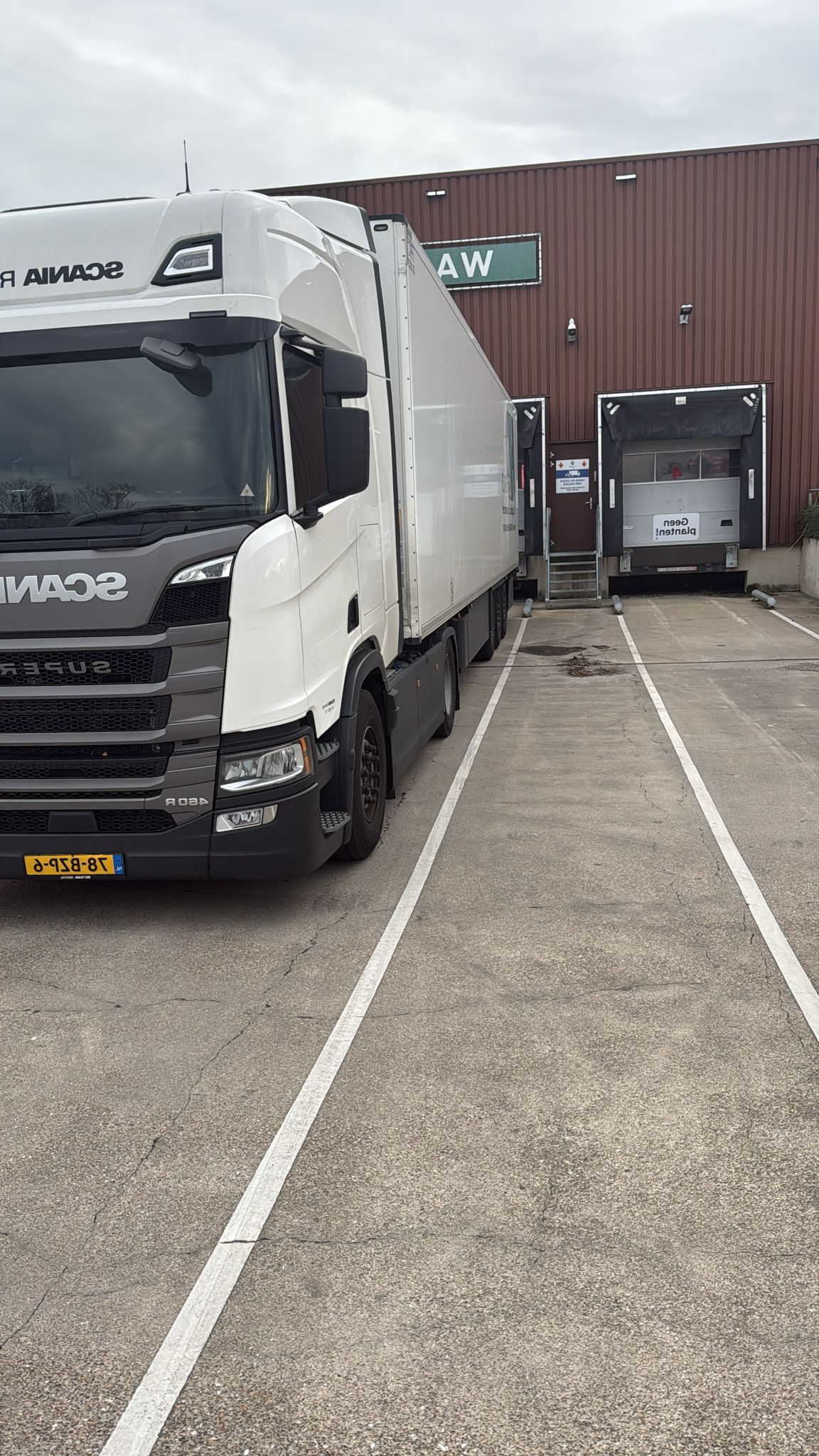 Witte vrachtwagen bij een laadperron; de vrachtwagen en het perron bevinden zich buiten op een betonnen ondergrond.