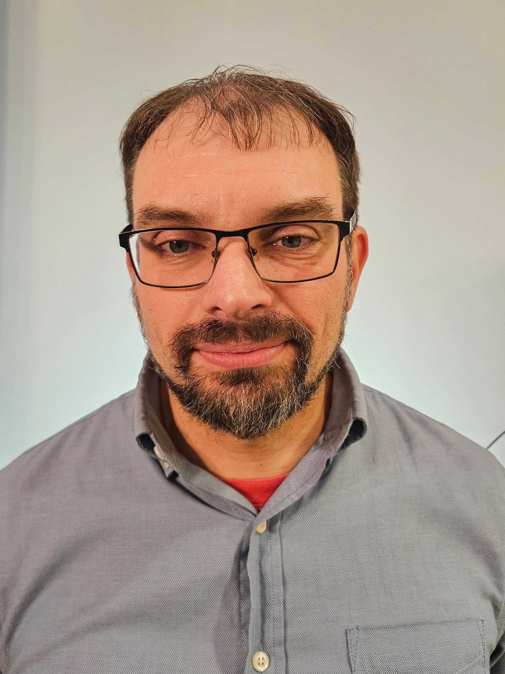 Man with glasses and beard, wearing a gray shirt, looking at the camera.