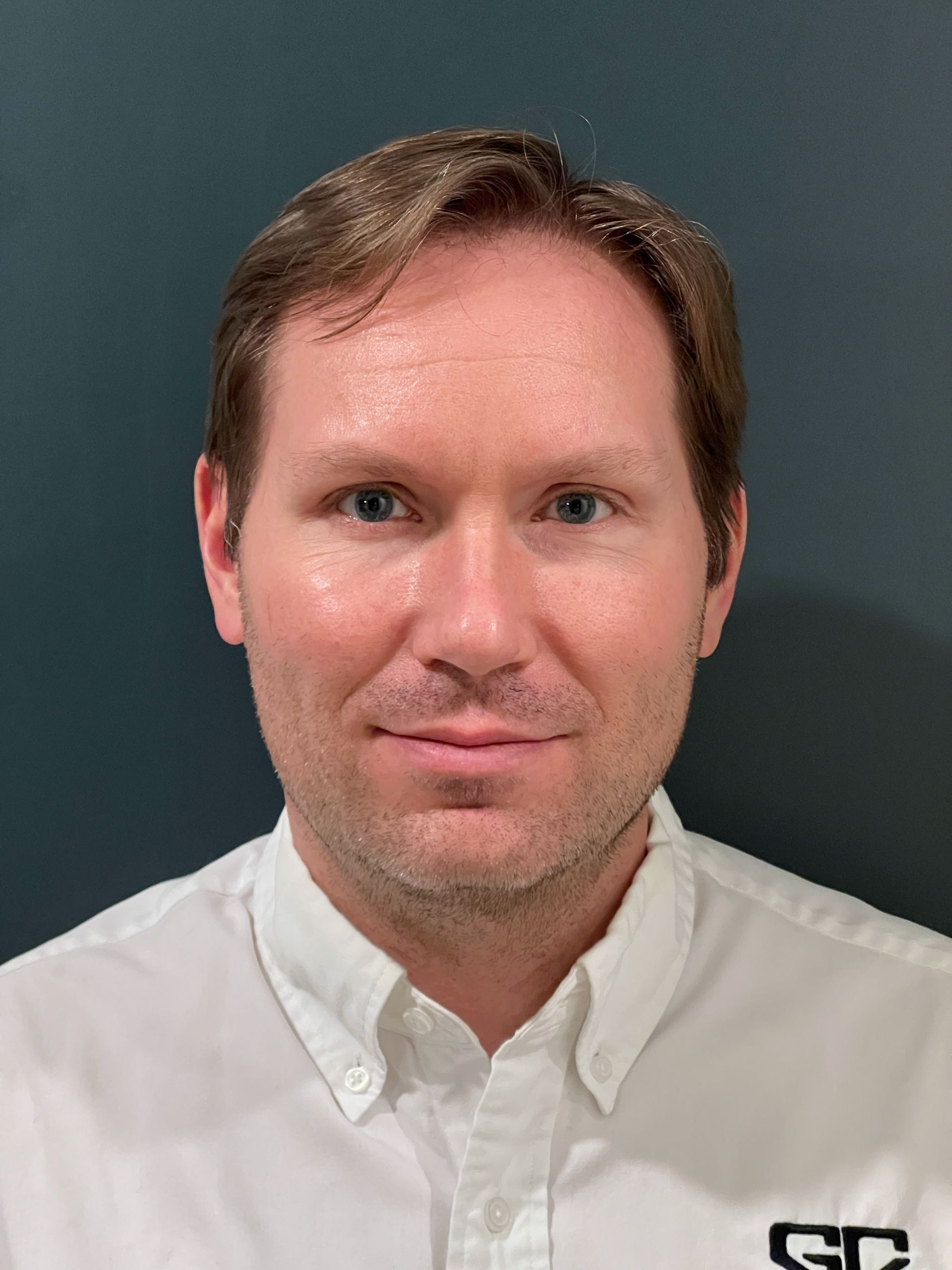 Man in white shirt smiles, headshot against a blue-gray background.
