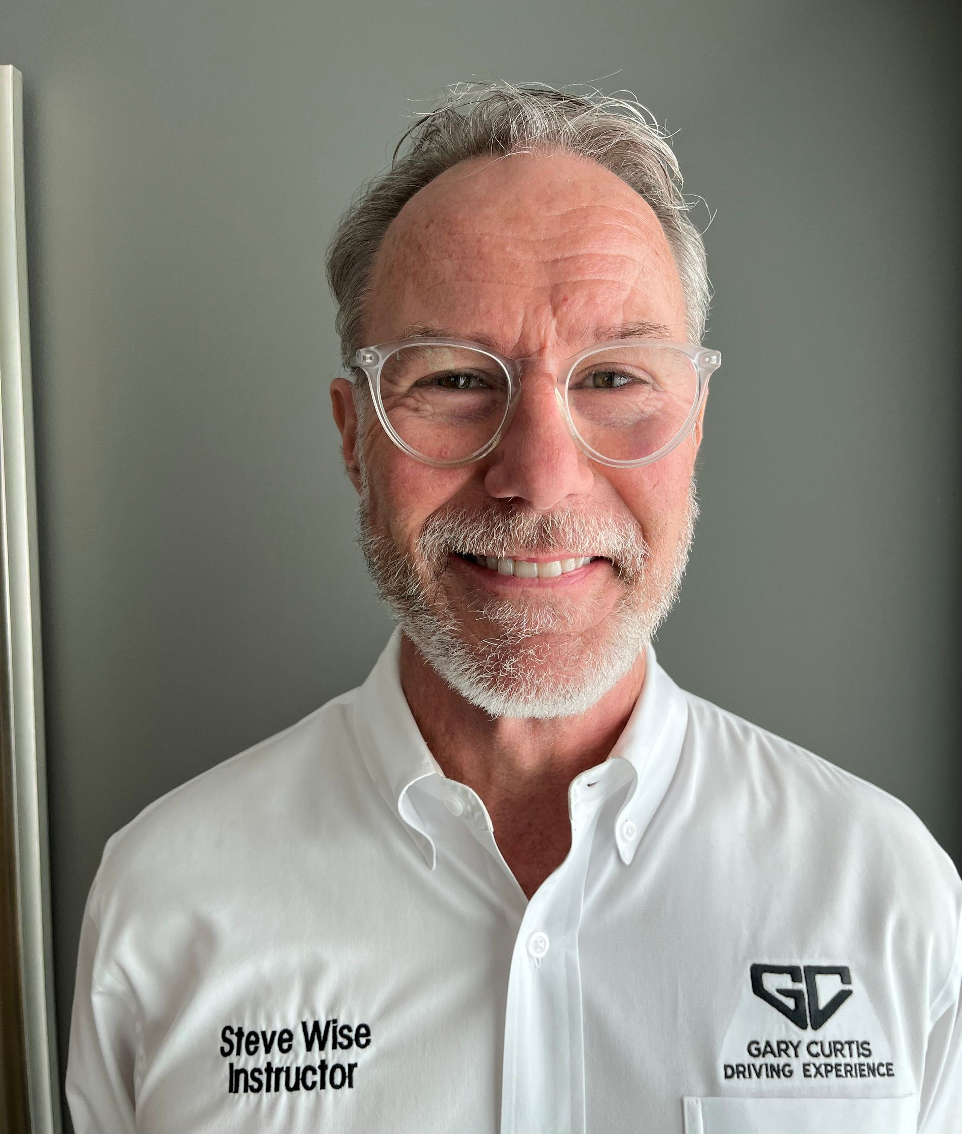 Man with glasses wearing a white shirt with text, smiling at the camera.
